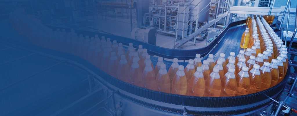 Bottles filled with orange liquid moving through a production line in a facility. 