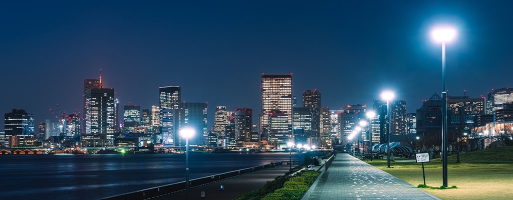 City skyline at night with a sidewalk illuminated by streetlights and text on the left side of the image. 